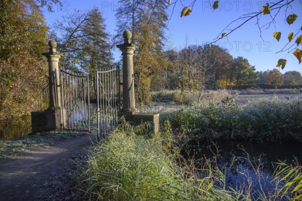 An open iron gate in a frosty garden, surrounded by autumnal colours and sunlight, borken, North