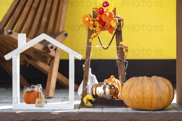 Autumn decor on porch of yellow house outside of pumpkin, lantern, garlands and figure of home and