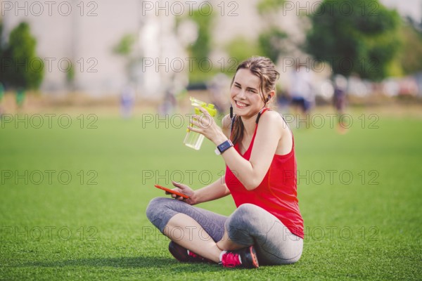 Theme sport health. beautiful young girl sitting resting on green grass lawn stadium using