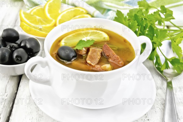 Soup saltwort with lemon, meat, pickles, tomato sauce and olives in a white bowl, towel, parsley on
