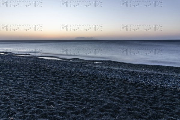 Morning atmosphere, sunrise over the sea, view from the lava beach to the island of Anafi, long