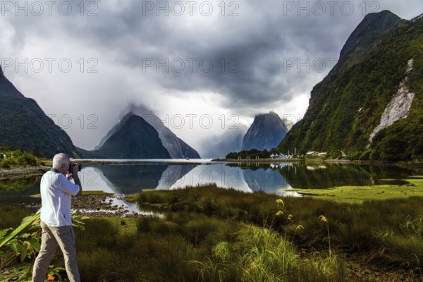 New Zealand. The famous ocean fjord Milford Sound. The gray-haired tourist photographs a