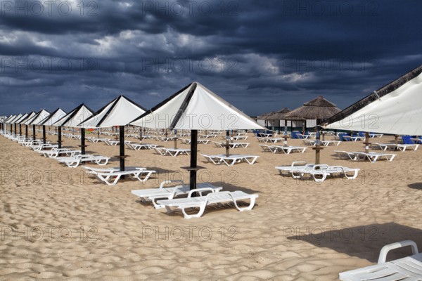 Different parasols and sun loungers on the empty beach on Tavira island before storm, Algarve.