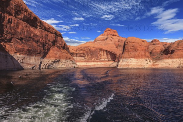 The foamy trace from powerboat crosses emerald waters. Hills from red sandstone surround the lake.