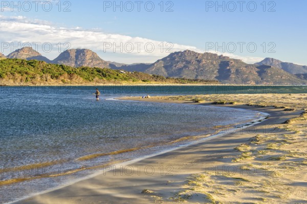 An angler in the shallow water on the Nine Mile Beach near Swansea with the Freycinet National Park