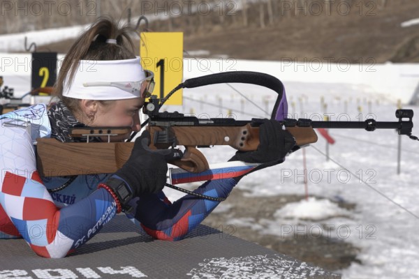 Sportswoman biathlete aiming, rifle shooting prone position. Biathlete Victoria Petrova Saint