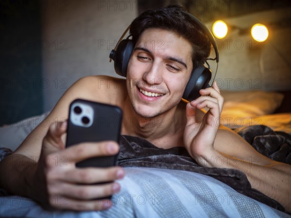 Glad male in headset smiling and text messaging on mobile while listening to favorite song and