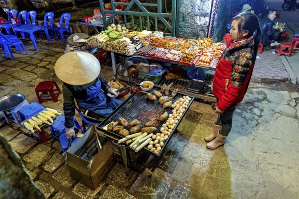 A busy street market with a stall selling grilled food surrounded by visitors, restaurant in the