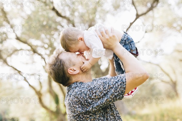 The father holds his son above him, they touching their noses, the son holds the father by the