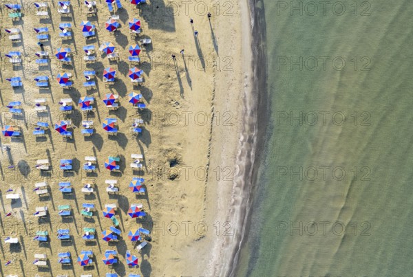 Aerial view of sandy beach with colorful umbrellas, people walking in the bay with transparent blue