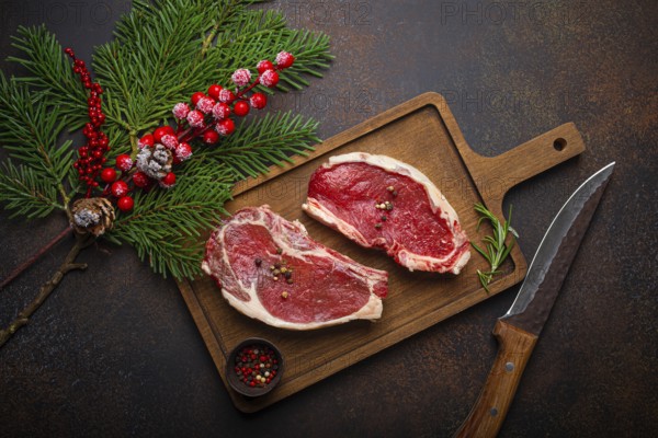 Two raw uncooked meat beef steaks on wooden cutting board with knife and seasonings on dark rustic