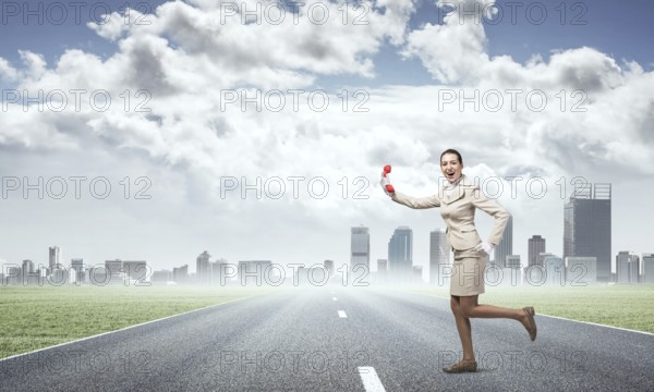 Woman running outdoor with vintage red phone. Expressive secretary with telephone on background