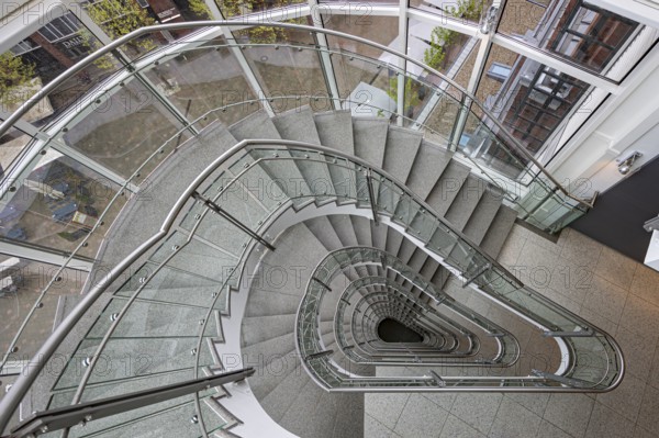 A modern spiral staircase with glass railings and a triangular shape in a bright room, Free and