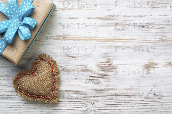 Flat lay cute composition with handmade fabric heart. Gift box with ribbon bow on wooden table.