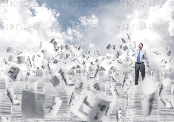 Businessman keeping hand with book up while standing among flying papers with cloudly skyscape on