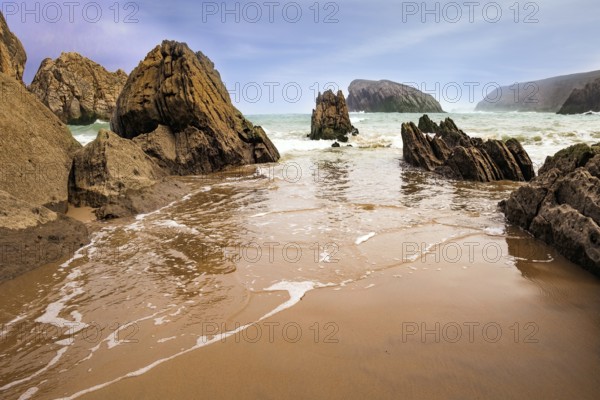 The smooth wet sand of the beach reflects the rocky boulders. The Playa de la Arnia beach.