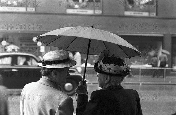 Umbrellas in the 1950s. The rain is pouring and two elderly ladies is seen holding an umbrella over