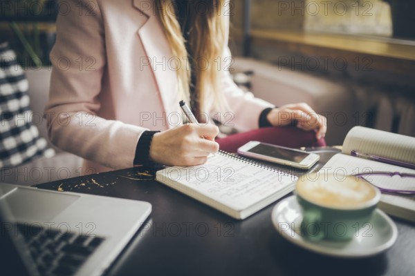 Close up caucasian woman hand on wooden table inside cafe makes notes in notebook. Subject