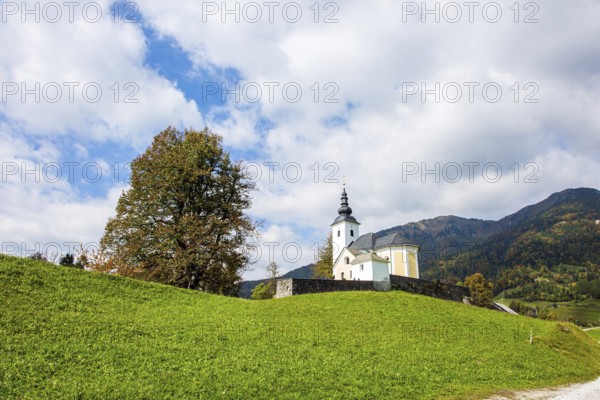White church and bell tower on a hill near the small village. Green grassy lawns in a mountain