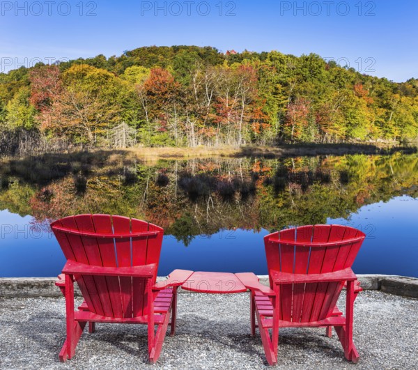 Red plastic loungers on the shore of the pond. Foliage of forests is reflected in the pond.