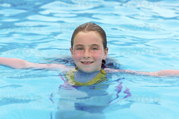 Blond kid girl swimming in the pool with sun tan red cheeks