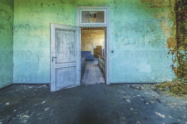 Open wooden door in a dilapidated room with peeling green wall paint, Prison H11, Lost Place,
