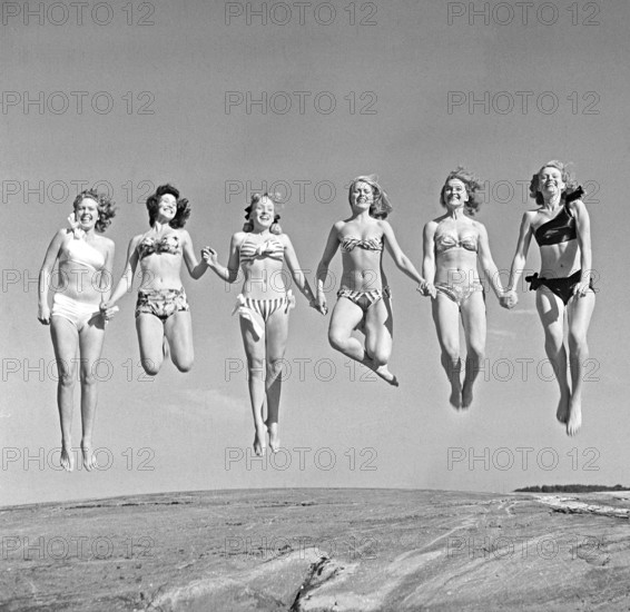 1940s summer. A group of young women in their bikinis are happy on this summer's day, jumping of