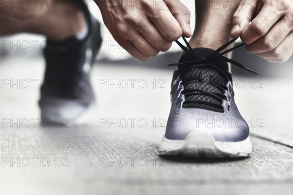 Cropped image of hands tying shoelaces on sneaker, running surface background. Hands of sportsman