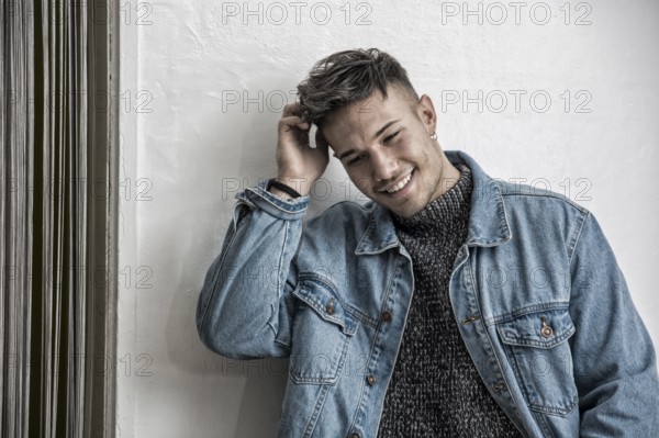 Handsome white asian young man wearing blue denim jacket, standing on light background against wall