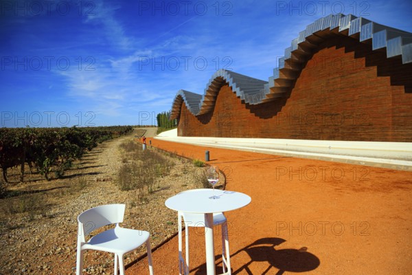 Table and chairs for tourists. Fragment of the facade. Wave-shaped winery roof. Winery - bodega