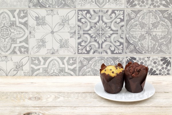Two tempting muffins on a white plate against a vintage tile backdrop create an inviting scene to