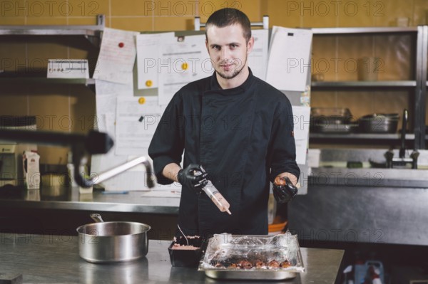 Theme cooking. A young Caucasian man in black uniform and latex gloves at a restaurant in the