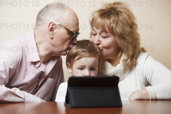Grandparents kissing their little grandson who is busy with touchpad