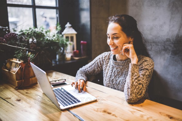 Beautiful young brunette woman using a laptop at coffee shop at a wooden table near window typing