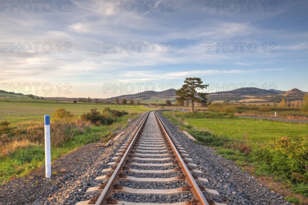 Old Railway tracks running through a field stretch to rural countryside at sunset. Single railway