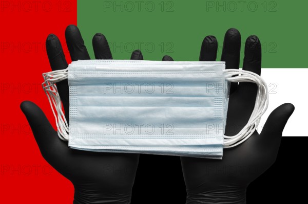 Doctor holds medical face mask in hands in black gloves on background colors national flag of
