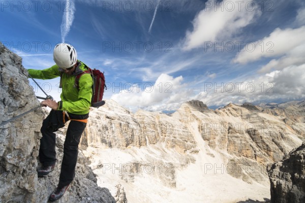 handsome male climber on a steep and exposed rock face climbs a Via Ferrata in Alta Badia in the