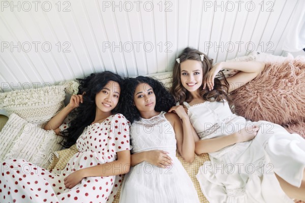 Beautiful multi ethnic girls have fun together, relax and lying on bed inside the camper van. Women