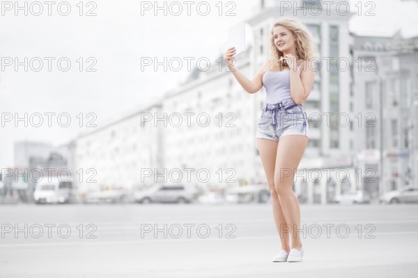 Happy young woman with vintage music headphones around neck taking selfie with tablet PC and