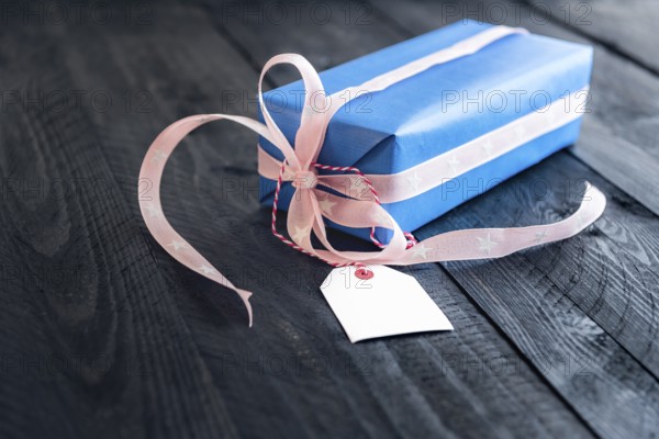 Classy blue gift, tied with pink ribbon and bow, with an empty label tied to it, on an old wooden
