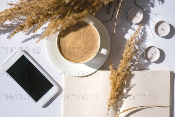 Pampas grass and white cup with coffee. Mobile phone with black screen. Checking social media