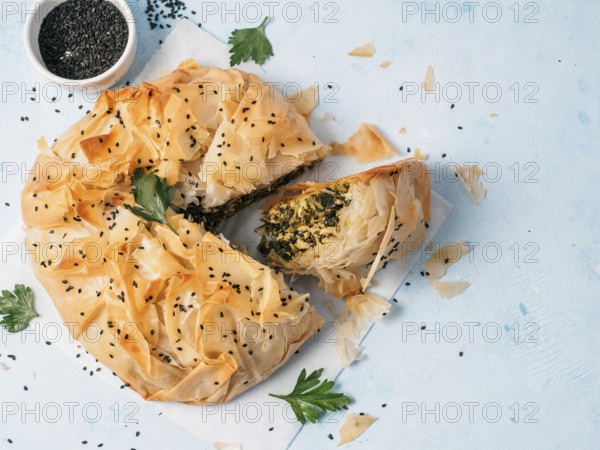 Greek pie spanakopita on white baking paper over blue background. Ideas and recipes for vegetarian