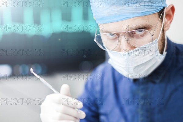 A serious surgeon with glasses and a mask, holding a tool in a medical setting