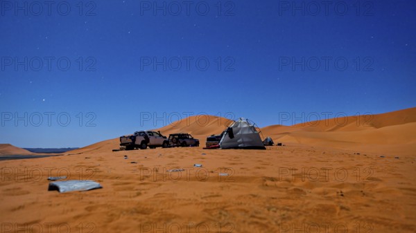 Camping scene in the desert under a starry night sky with tents and vehicles, tent camp in the