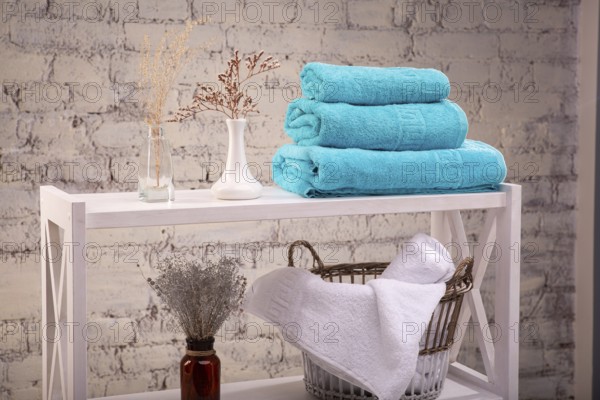 Rack with a stack of three colour turquoise towels and baskets with clean white towels and toilet