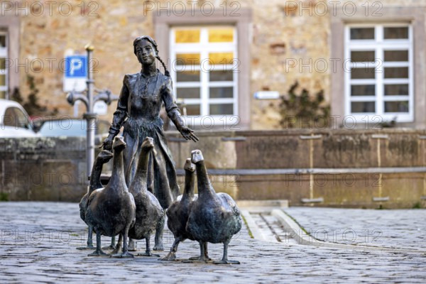 Statue of a girl with geese in front of a historic building, a parked car in the background, The