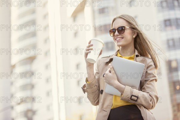 Beautiful young businesswoman with a disposable coffee cup, drinking coffee and holding a tablet in