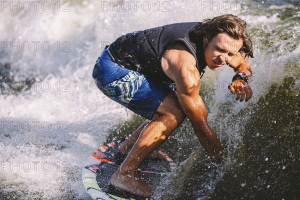 Young athletic man with long hair wakesurfing on waves of river in sunny summer weather. Ttheme