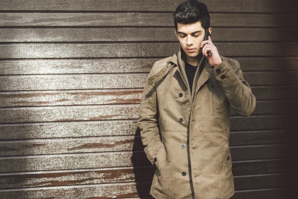 Portrait of a model young mulatto male Turkish Mediterranean race brunet in coat uses hand phone