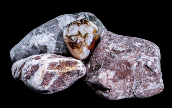 A smooth, polished agate gemstone with intricate banding patterns rests on a group of textured,